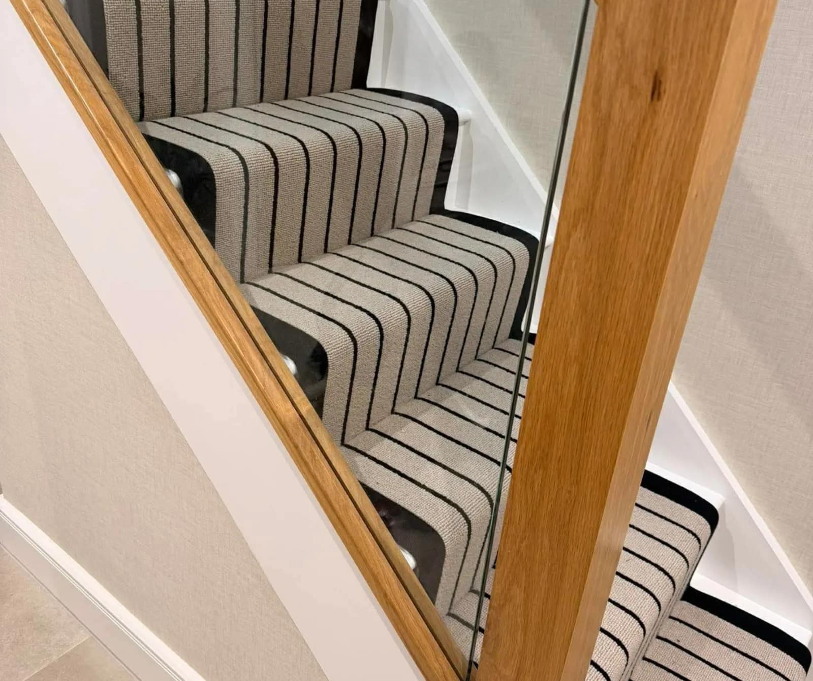 A striped stair runner fitted against an oak handrail and white painted risers