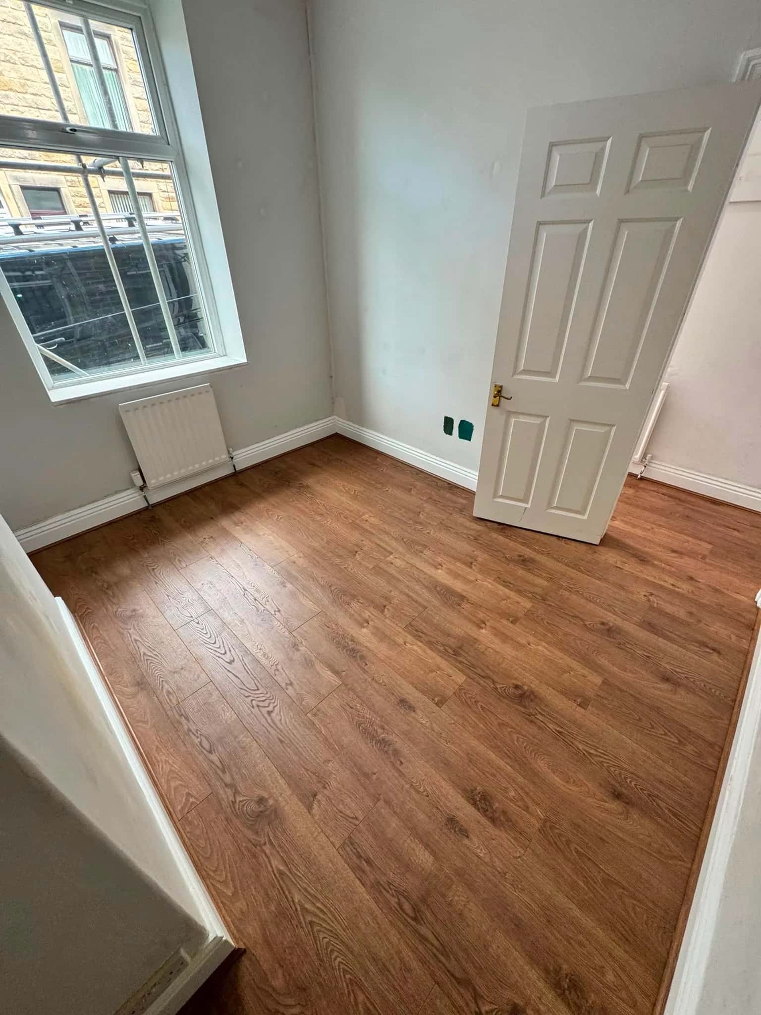 Oak effect laminate fitted in an empty room with a sash window and a radiator