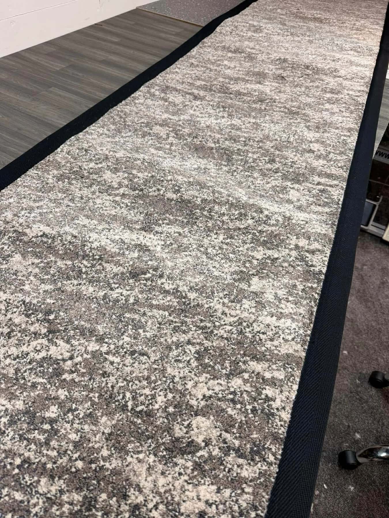A grey patterned rug bound with a black border