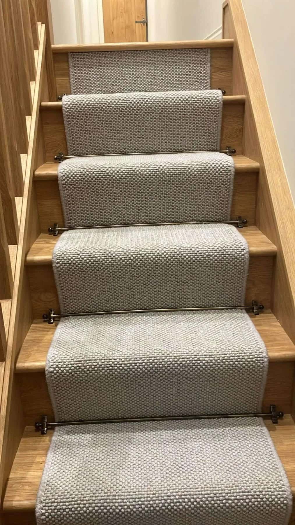 A woven stair runner held by brass rods on oak treads