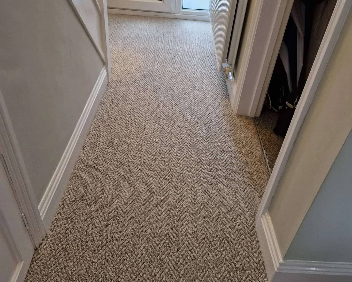 Herringbone patterned carpet fitted the length of a hallway between painted doors