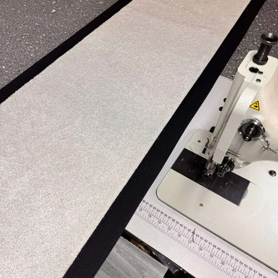 A carpet edge running through the binding machine on the workshop bench