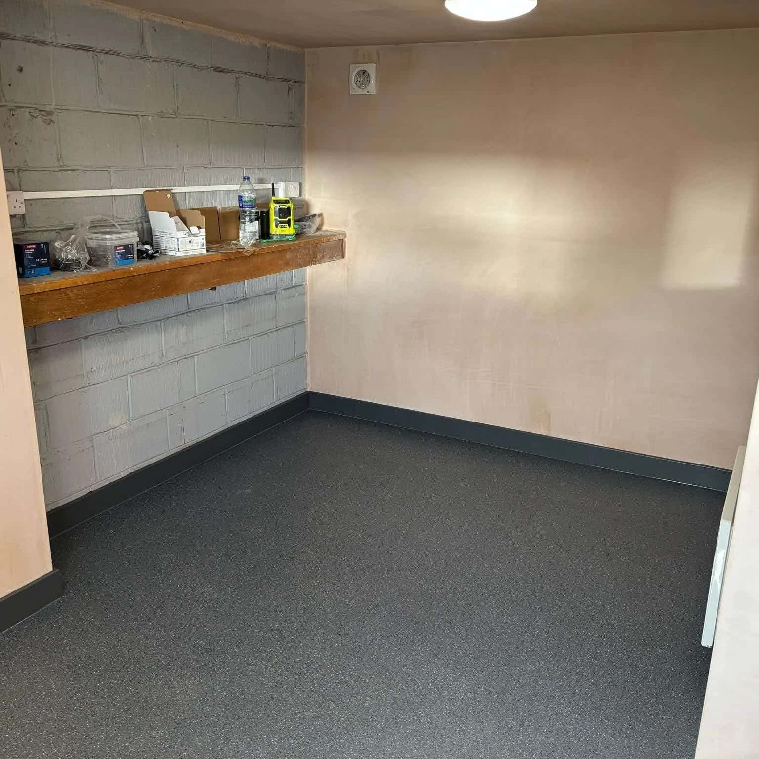 Grey contract sheet vinyl fitted across a back-of-house room, carried up into a coved edge against block walls