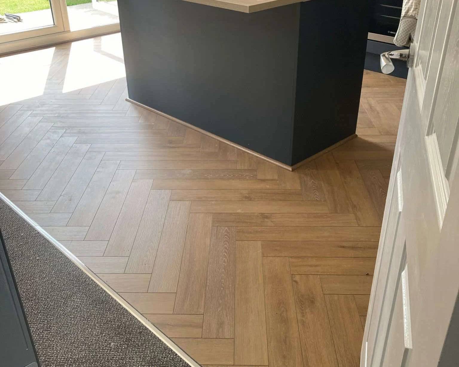 Herringbone wood effect flooring laid through a kitchen up to a dark island unit