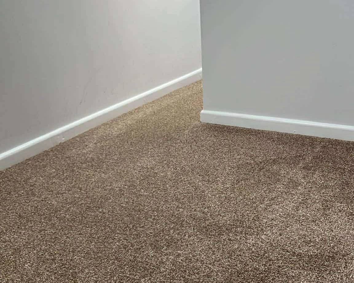 Brown carpet fitted wall to wall through an empty room, cut in to the skirting