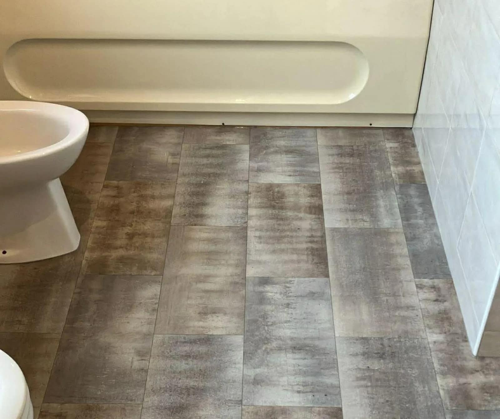 Plank effect vinyl flooring fitted in a bathroom, running cleanly up to the bath panel and pedestal