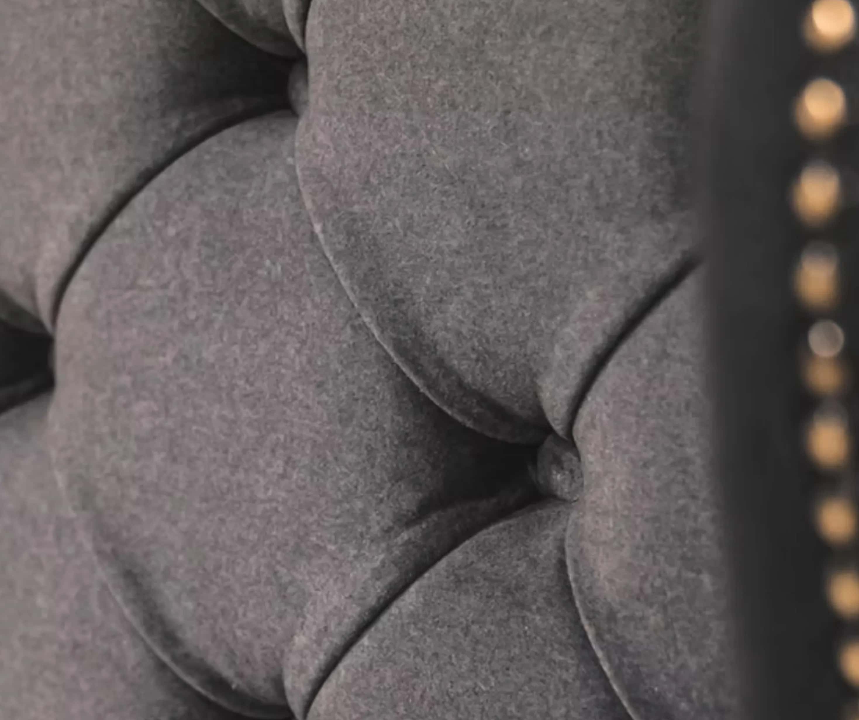 A close view of a deep buttoned grey upholstered headboard with a studded edge