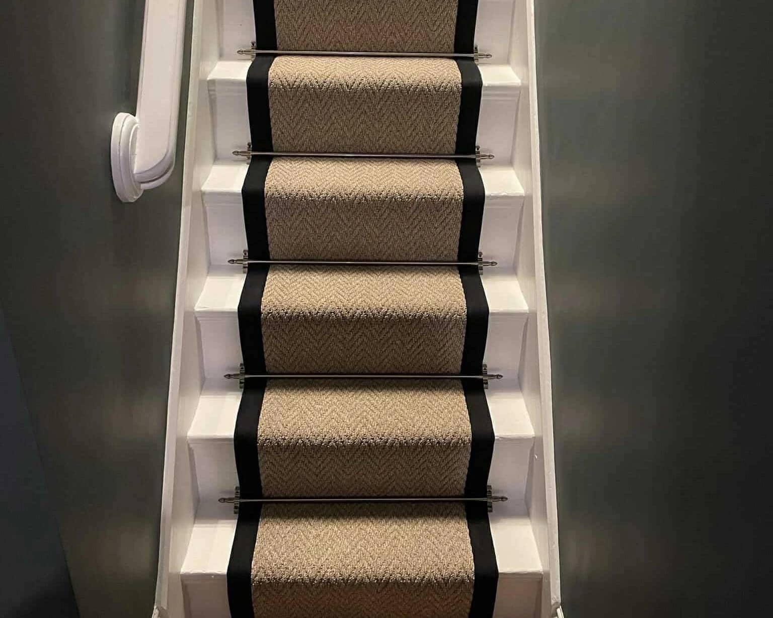 A bound stair runner with black borders and stair rods against a dark wall
