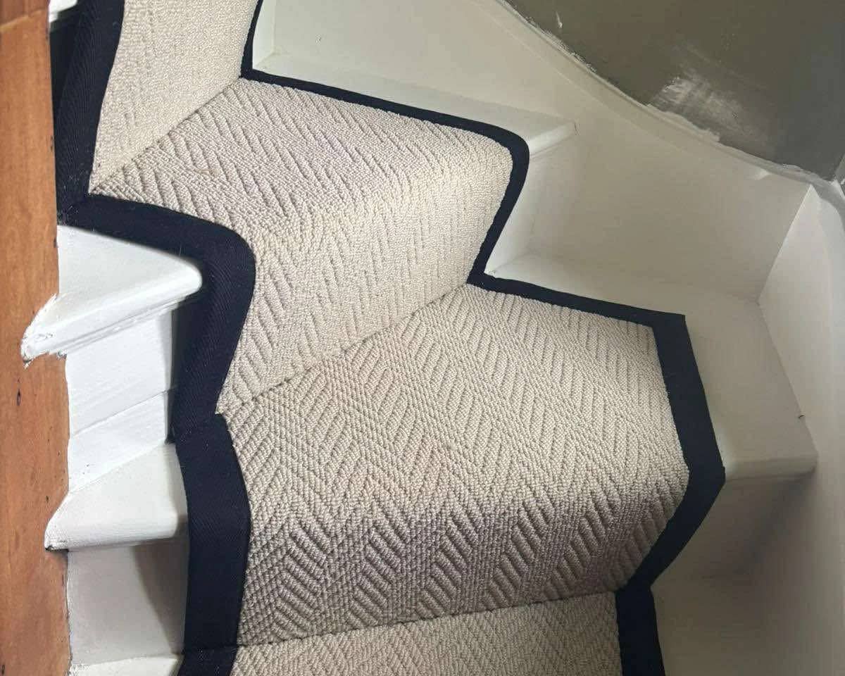 A cream stair runner with a navy bound border, fitted around a winding turn